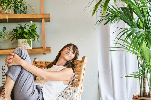Smiling woman hugging knee while relaxing on chair at home