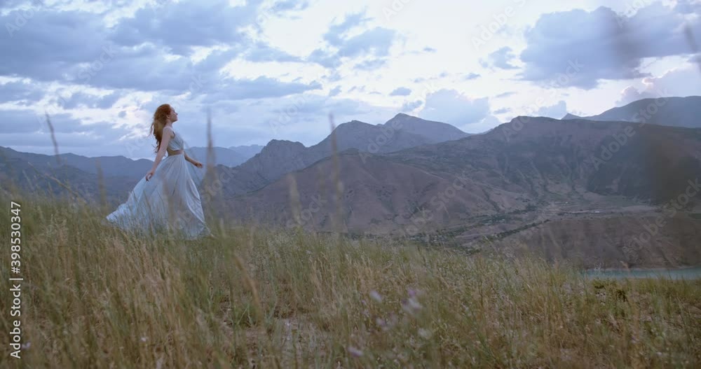 Young beautiful girl with red hair wearing white dress walking on top of a mountain facing wind blowing her hair and dress - freedom, adventure, harmony 4k footage Young beautiful girl with red hair wearing white dress walking on top of a mountain facing wind blowing her hair and dress - freedom, adventure, harmony 4k footage