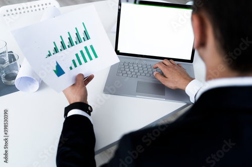 Young businessman analyzing growth graph through laptop while planning at creative workplace photo