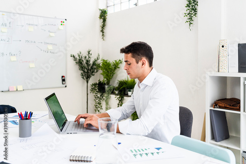 Handsome businessman using laptop while planning strategy at desk in creative workplace