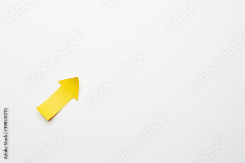 Right-up yellow paper arrow curved up of both sides which lies on the solid white paper background, showing growth of stock market or up direction © Antonio