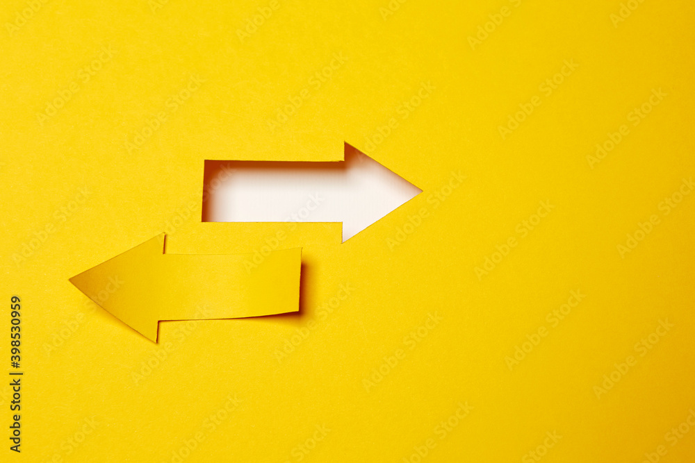 Two opposite left/right arrows, one cutted from the yellow paper curved up of two sides on the yellow paper background other made as an arrow shaped hole in the background with white paper underlay Two opposite left/right arrows, one cutted from the yellow paper curved up of two sides on the yellow paper background other made as an arrow shaped hole in the background with white paper underlay