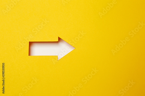One right direction arrow, cut out as an arrow shaped hole in the yellow paper background with white paper underlay © Antonio
