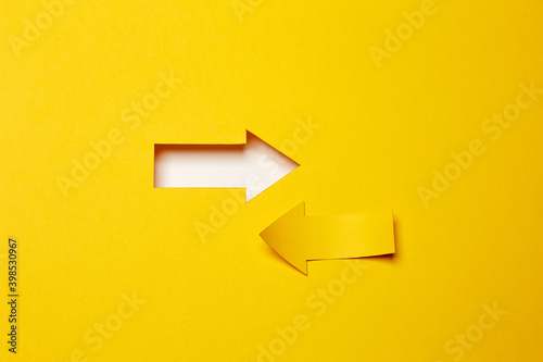 Two opposite left/right arrows, one cutted from the yellow paper curved up of two sides on the yellow paper background other made as an arrow shaped hole in the background with white paper underlay © Antonio