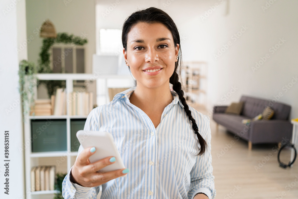 Smiling young woman using smart phone while standing at home Smiling young woman using smart phone while standing at home