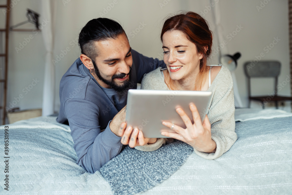 Smiling couple using digital tablet while lying on bed at home Smiling couple using digital tablet while lying on bed at home