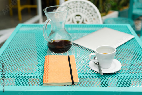 Table with notepad, laptop, coffee cup and pot at cafe photo