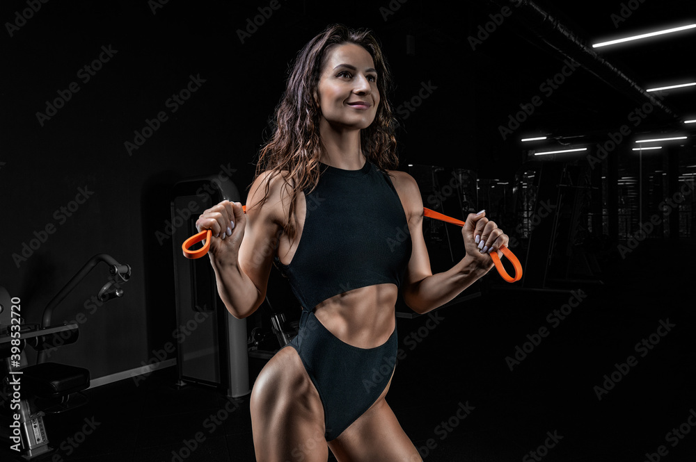 Tall athletic woman posing with gymnastic elastic bands in the gym