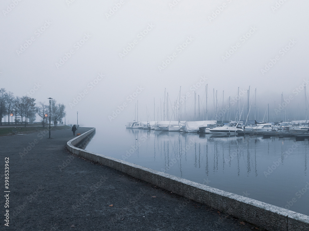 The empty waterfront and sailing harbor are shrouded in the evening fog.