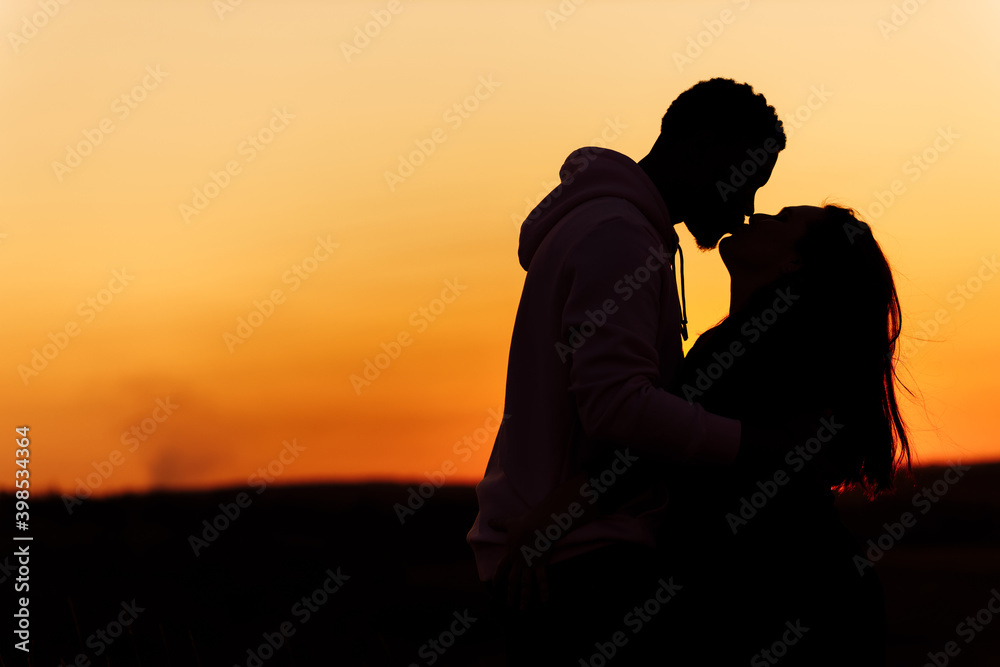 Silhouettes of lovely couple, handsome man kiss beautiful woman at sunset, enjoy tender moments, caring husband and loving wife spend time together, weekends outdoors concept