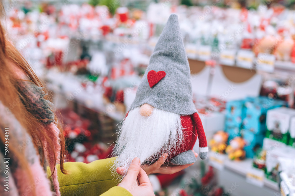 The girl holds Tomte in her hands. against the background of the counter of the Christmas New Year's shop.