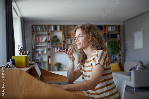 Woman talking on mobile phone while sitting by desk at home