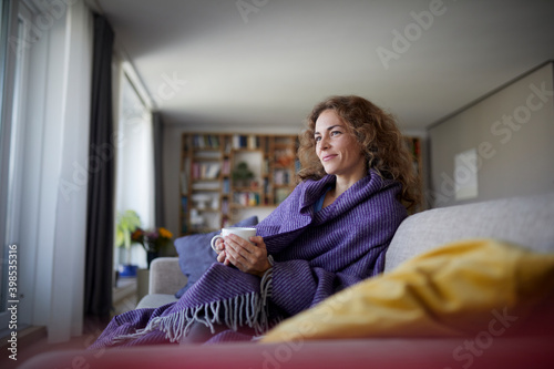 Smiling woman wearing shawl drinking coffee while sitting on sofa at home