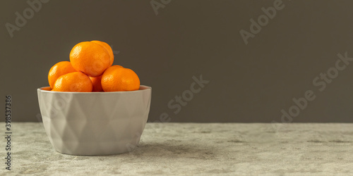 Fresh organic citrus mandarin oranges fruit in a gray bowl on a gray stone background. Selective focus, side view and copy space. Banner.