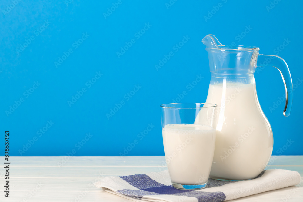 Glass and pitcher of milk against blue background Glass and pitcher of milk against blue background