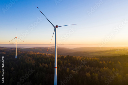 Wind turbines standing in autumn forest at dusk photo