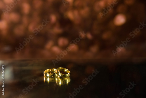 Golden wedding rings on sparkle bokeh background. Selective focus with copy space for text. Wedding card and invitation background. Pink color. 