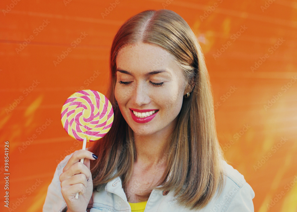 Summer colorful portrait of happy smiling young woman with lollipop over an orange background