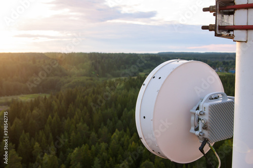 Cellular microwave system. Wireless directional communication antenna of radio relay link based on telecommunication tower metal construction. Pine tree forest and cloudy sky background. photo