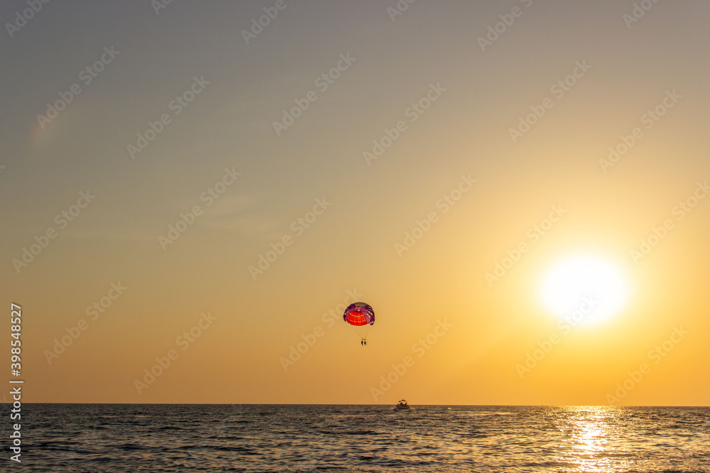 Siluet people flying on a parachute  in the evening sky.    Colourful sunset over the sea..