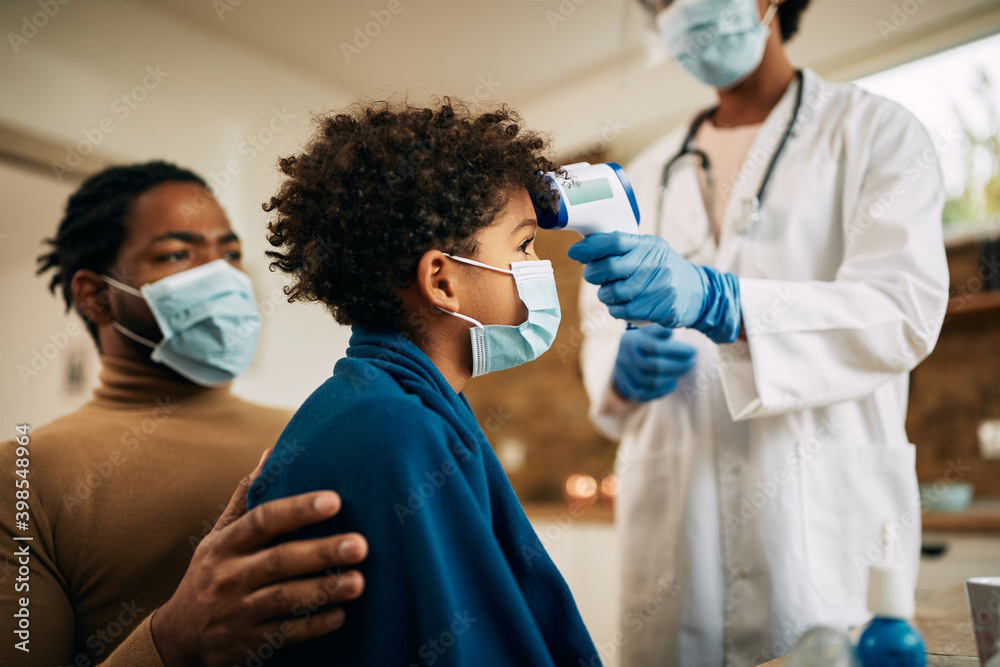 Small black boy getting his body temperature measured by family doctor during home visit. Small black boy getting his body temperature measured by family doctor during home visit.