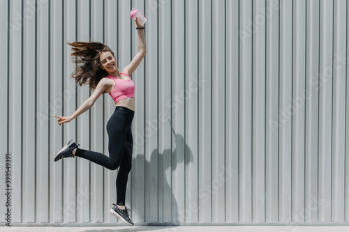 Outdoor fitness, training, gym workout on fresh air. Young woman with water bottle jumping and running. Girl in sportswear exercising outdoors.