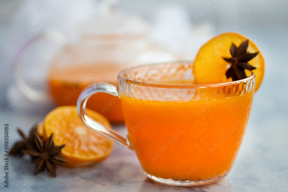 Sea buckthorn tea in a glass cup with orange and spices and a glass teapot on a light blue marble background. Sea buckthorn tea in a glass cup with orange and spices and a glass teapot on a light blue marble background.