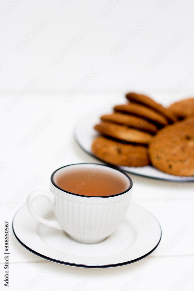 A cup of tea and oatmeal cookies. Breakfast. Tea drinking. White wooden background. A cup of tea and oatmeal cookies. Breakfast. Tea drinking. White wooden background.