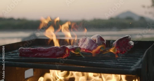 Tossing red chili peppers onto a park grill in slow motion. The fresh, raw chile peppers bounce on the flaming grate. Flames represent the heat of the spicy red chili peppers. 