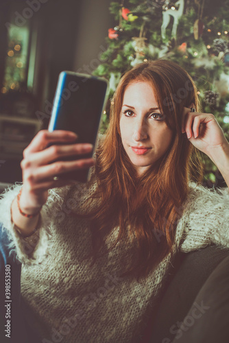 Cute and young red-haired girl taking a selfie on the sofa in front of the christmas tree photo