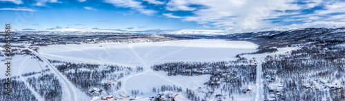 Scenic aerial view on Tarna Vilt village and Joesjo lake in Swedish Lapland in winter cover, frosty sunny day. Roads, houses, frozen lakes, birch trees with Scandinavian mountains at background photo