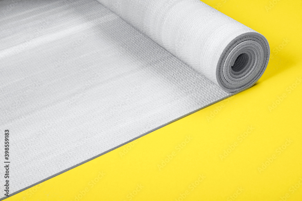 Gray color exercise mat on yellow background with copy space. Trendy colors 2021 year. Yoga practice, physical workout, pilates or fitness concept. Gray color exercise mat on yellow background with copy space. Trendy colors 2021 year. Yoga practice, physical workout, pilates or fitness concept.