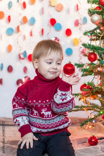 A child is holding a Christmas tree toy while sitting under an elegant Christmas tree. Children's emotions. Christmas and New year.