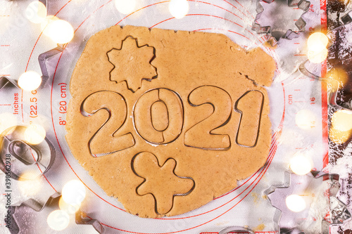 Woman hand cutting cookies, year 2021 on dark board with baking flour. rolling pin, flour and shape of new year figures. New year ornament food background. Homemade cooking preparation for cookie.