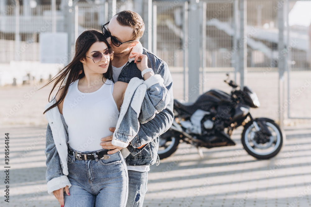 Sexy girl and guy hugging and kissing on the background of a sports motorcycle standing in the parking lot near a large football stadium