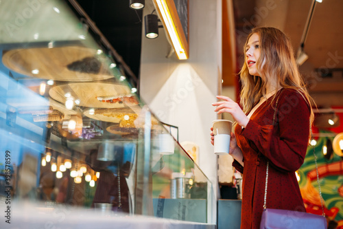 Tableau sur toile young beautiful woman with cup of coffee in her hands is standing at window, cho