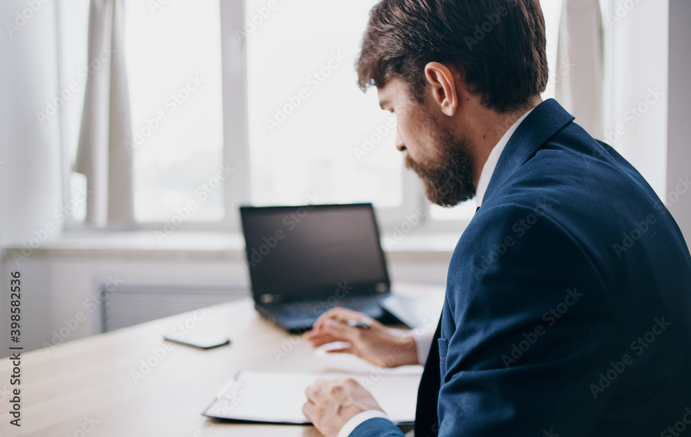 Business man in a suit at the table in the office laptop in the background documents model Business man in a suit at the table in the office laptop in the background documents model