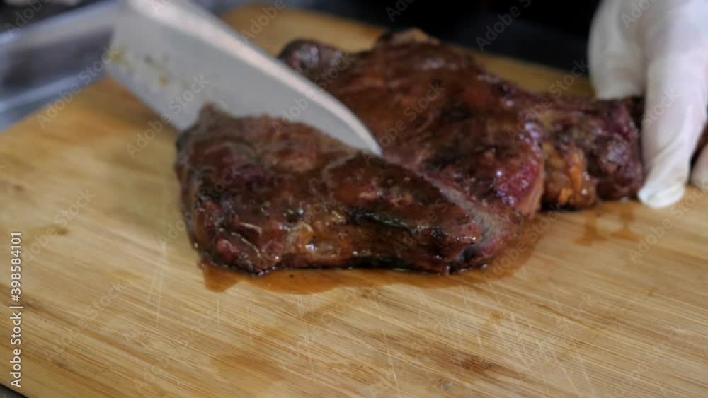 Process of cutting tomahawk steak with a large knife on wooden board. Juicy meat is separated into even pieces. Process of cutting tomahawk steak with a large knife on wooden board. Juicy meat is separated into even pieces.