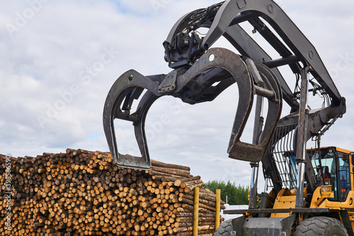 bucket a forestry grapple loader against the background of a stack of logs outdoors