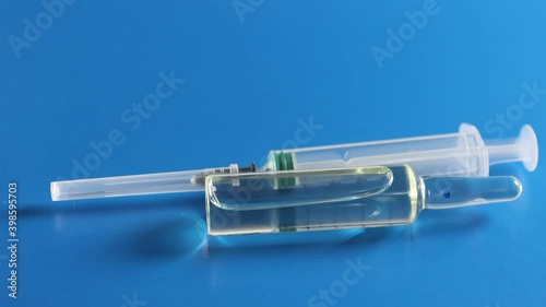 An ampoule with a vaccine and a syringe are on a blue background. The concept of vaccination against coronavirus.