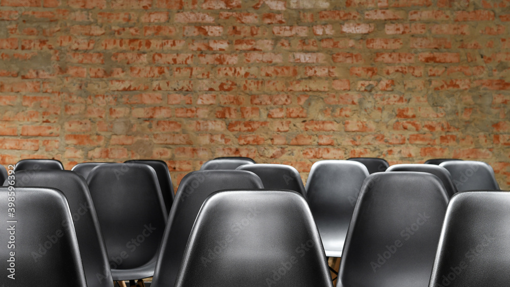 Rows of empty black chairs with red brick wall background. Copy space.