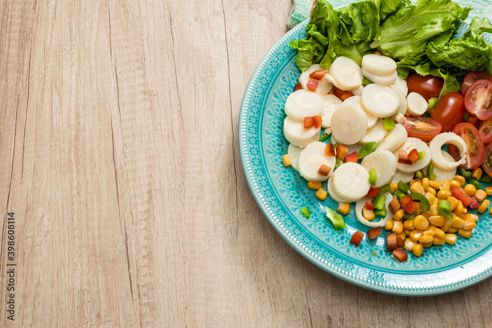 Fresh and exquisite salad of palm hearts cut into slices, cherry tomatoes, corn kernels, red pepper, lettuce in a vintage light blue plate on a wooden table ready to taste. concept healty food. Fresh and exquisite salad of palm hearts cut into slices, cherry tomatoes, corn kernels, red pepper, lettuce in a vintage light blue plate on a wooden table ready to taste. concept healty food.