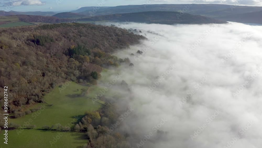 Aerial view flying over mist and fog around a small forest and rural farmland (Wales, UK) Aerial view flying over mist and fog around a small forest and rural farmland (Wales, UK)