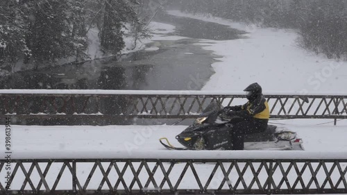A snowmobiler on a bridge in the woods 