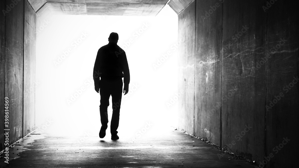 silhouette of man, shoulders slumped walking out of a dark tunnel towards a bright light.