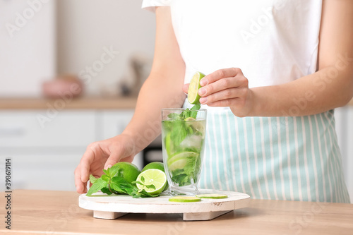 Woman and glass of fresh mojito in kitchen