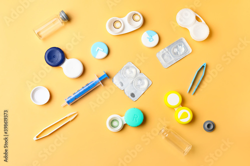 Containers with contact lenses, solution, tweezers and syringe on color background