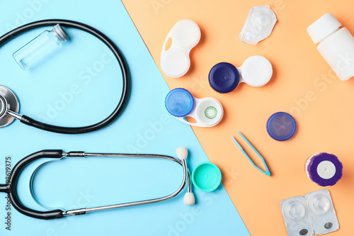 Containers with contact lenses, solutions, stethoscope and tweezers on color background