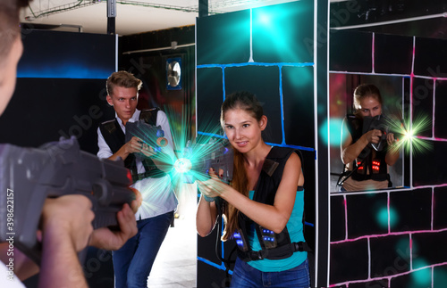 Two exciting players man and girl standing opposite each other with laser guns in dark laser tag room