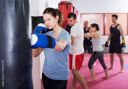 female beating boxing bag training in kickboxing gloves